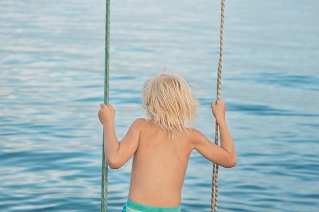 Blonde jongen rijdt touwschommel op zee