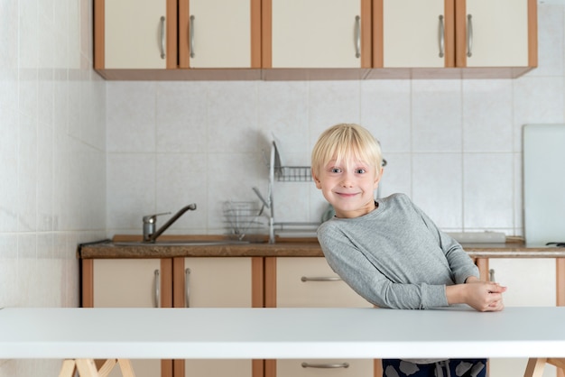 Blonde jongen staat in de keuken en glimlacht. Portret van blond kind in de keuken.