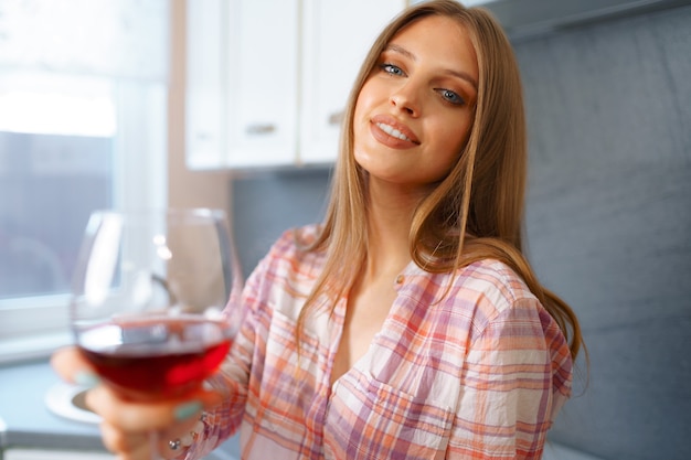 Blonde Kaukasische gelukkige vrouw met glas rode wijn die zich in haar keuken bevindt