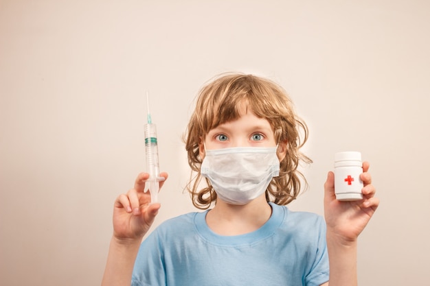 Blonde kid with surgical mask and holding syringe with vaccine and white jar with pills in his hands, infection spread and contamination concept