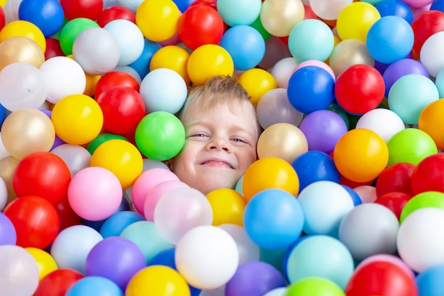 Blonde kleine jongen liggend op multi gekleurde plastic ballen in groot droog peuterbad in speelcentrum