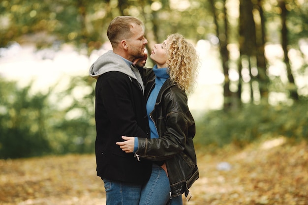 Blonde krullende vrouw en man staan in het herfstbos en knuffelen