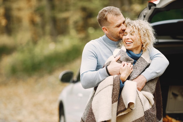 Blonde krullende vrouw en man staan in het herfstbos en knuffelen