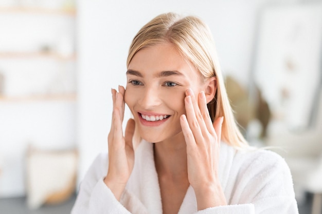 Blonde lady enjoys freshness of skin touching face in bathroom