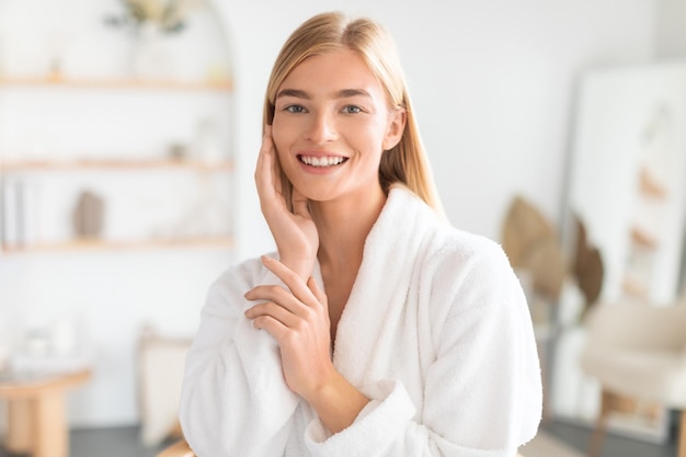 Photo blonde lady enjoys her skincare routine touching cheek in bathroom