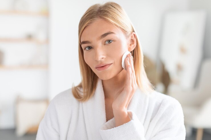 Photo blonde lady enjoys moment of skincare with cotton pad indoors