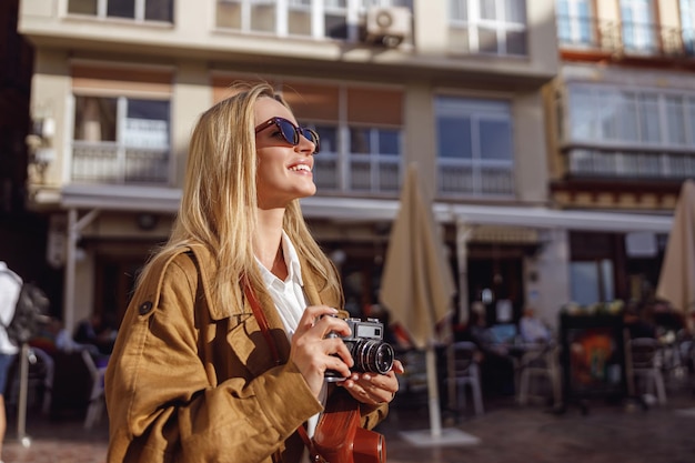 Фото Блондинка держит ретро-камеру, стоя на улице