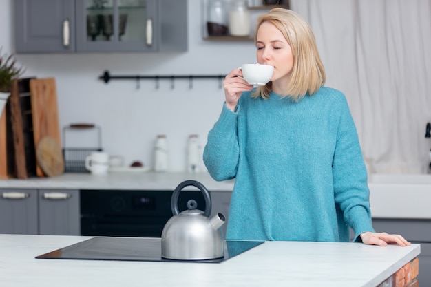 Signora bionda con una tazza di caffè in cucina