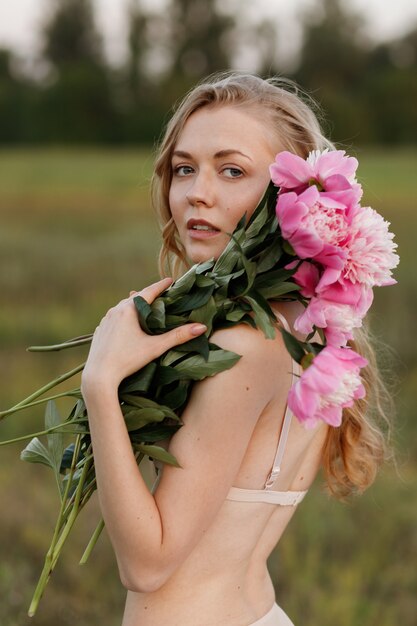 Blonde in lingerie holds a bouquet of peonies in summer