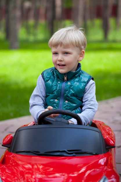 Foto un ragazzino biondo che guida una grande macchina giocattolo all'aperto