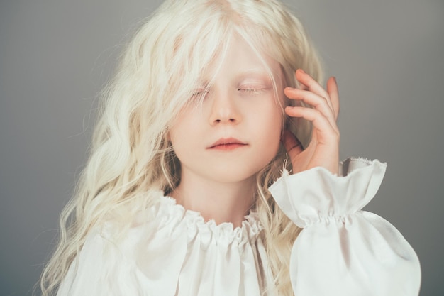 Foto bambina bionda. bellezza d'angelo. purezza del bambino. ritratto di adorabile bambino pacifico carino con capelli ricci occhi chiusi in camicetta vintage bianca isolata su sfondo grigio.