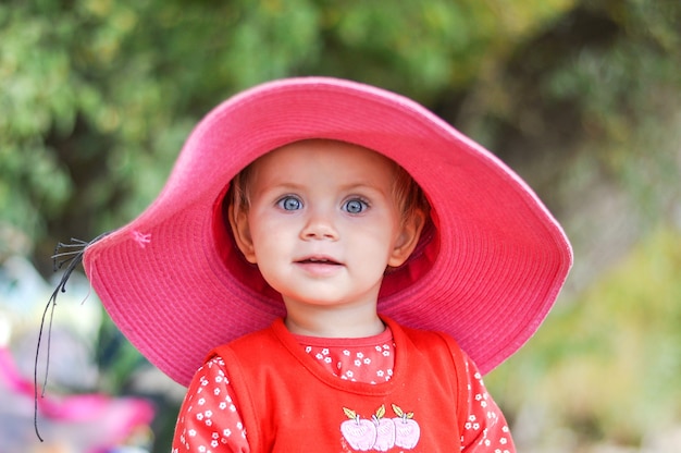 Blonde little girl in hat on the beach in a red dress in the spring