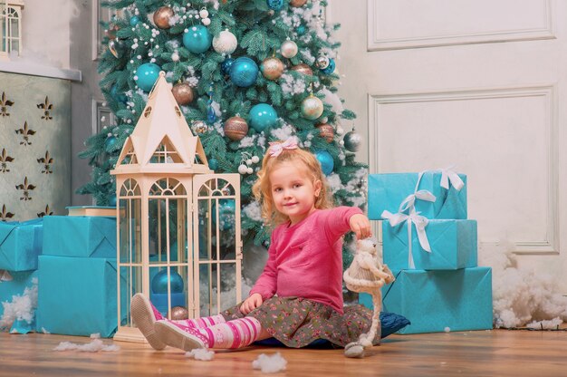 거의 장식 된 크리스마스 트리와 새해 선물에 앉아서 웃고있는 금발 소녀