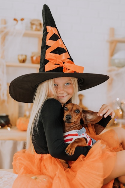 blonde little girl in a witch costume in huge witch hat and an orange puffy skirt Halloween concept