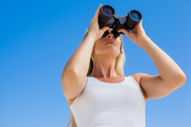 Photo blonde looking through binoculars on the beach