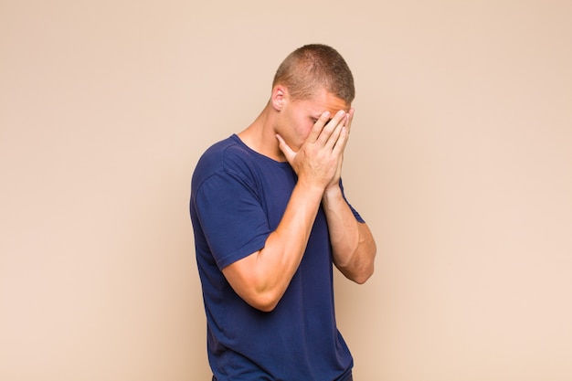 Blonde  man covering eyes with hands with a sad, frustrated look of despair, crying, side view