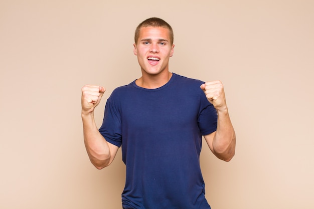 Blonde  man feeling happy, surprised and proud, shouting and celebrating success with a big smile