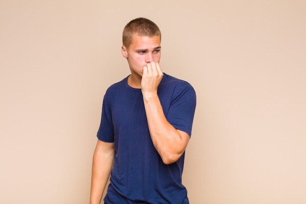 Blonde man feeling serious, thoughtful and concerned, staring sideways with hand pressed against chin