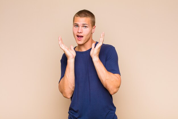 Blonde man feeling shocked and excited, laughing, amazed and happy because of an unexpected surprise