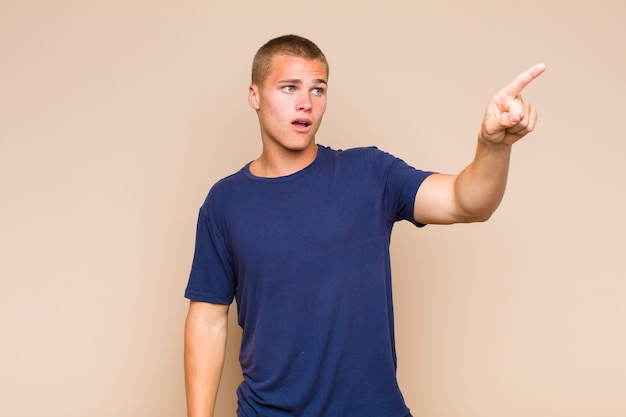 Blonde  man feeling shocked and surprised, pointing and looking upwards in awe with amazed, open-mouthed look