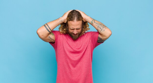 Blonde man feeling stressed and frustrated, raising hands to head, feeling tired, unhappy and with migraine