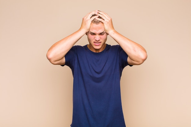 Blonde  man feeling stressed and frustrated, raising hands to head, feeling tired, unhappy and with migraine