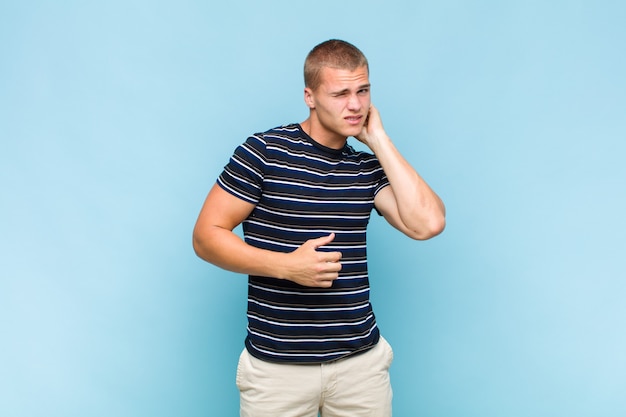 Blonde  man feeling stressed, frustrated and tired, rubbing painful neck, with a worried, troubled look