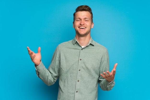 Blonde man over isolated blue wall smiling a lot