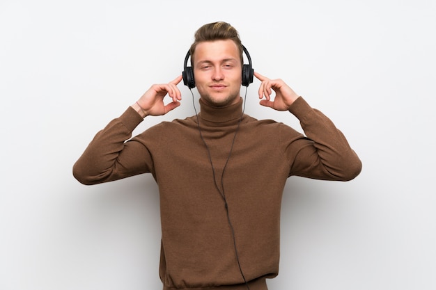 Blonde man over isolated white wall listening to music with headphones