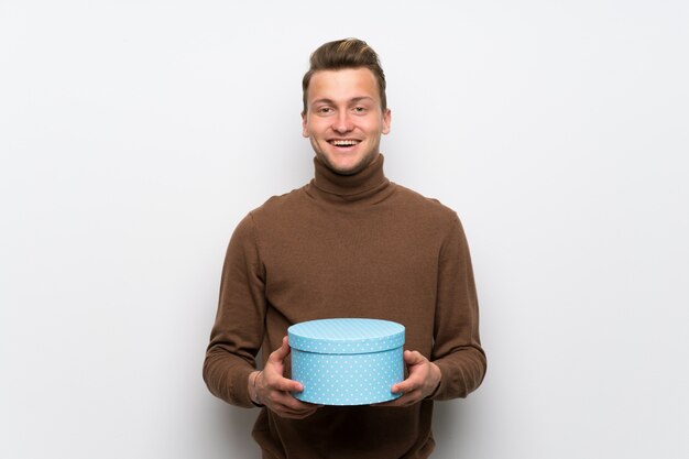 Blonde man over isolated white wall surprised because has been given a gift