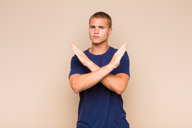 Foto blonde man kijkt geïrriteerd en ziek van je houding, zegt genoeg! handen voorover gekruist, zeggend dat je moet stoppen