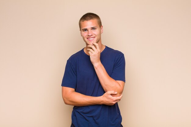 Blonde man looking happy and smiling with hand on chin