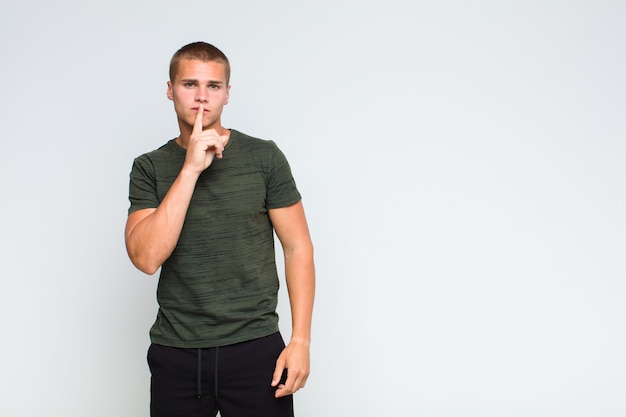 Blonde man looking serious and cross with finger pressed to lips demanding silence or quiet