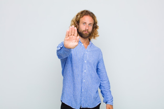 Blonde man looking serious, stern, displeased and angry showing open palm making stop gesture