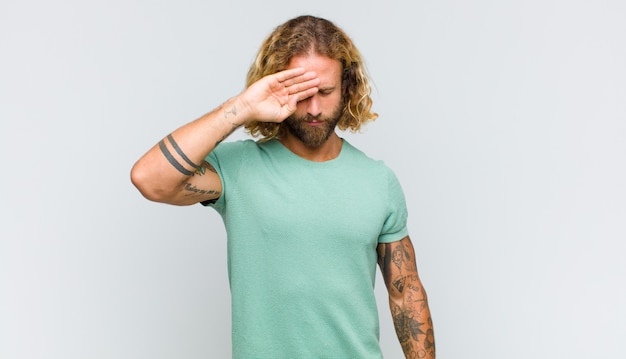 Blonde man looking stressed, tired and frustrated, drying sweat off forehead, feeling hopeless and exhausted