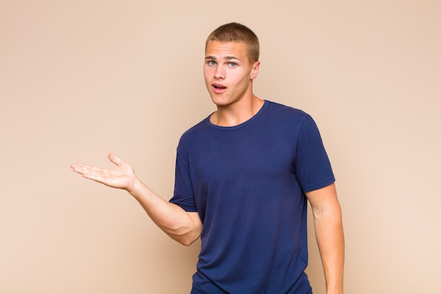 Blonde  man looking surprised and shocked, with jaw dropped holding an object with an open hand on the side