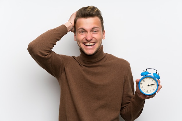 Blonde man over geïsoleerde witte muur rusteloos omdat het laat is geworden en vintage wekker bedrijf