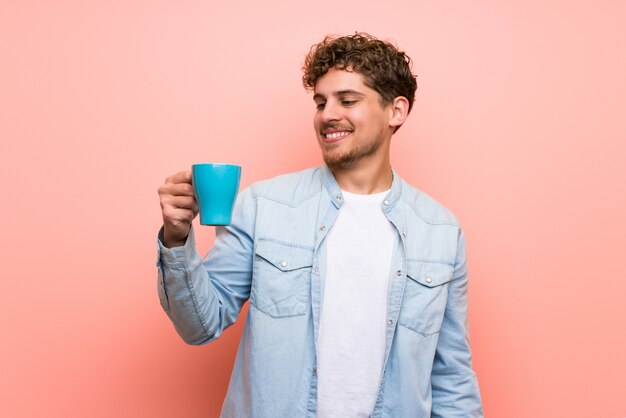 熱い一杯のコーヒーを保持しているピンクの壁の上の金髪の男