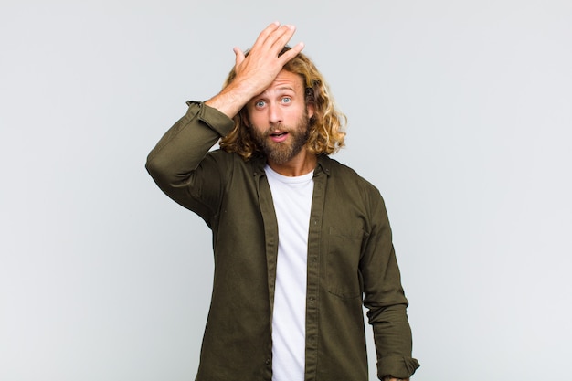 Blonde man raising palm to forehead thinking oops, after making a stupid mistake or remembering, feeling dumb