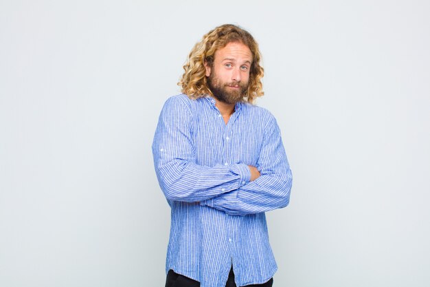 Blonde man shrugging, feeling confused and uncertain, doubting with arms crossed and puzzled look