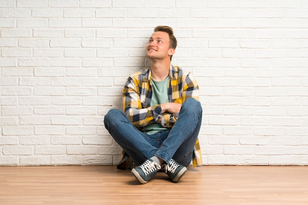 Photo blonde man sitting on the floor looking up while smiling