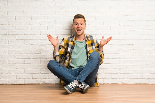 Blonde man sitting on the floor with shocked facial expression