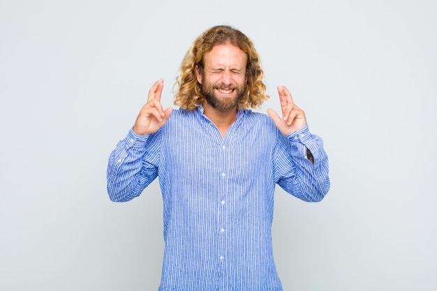 Blonde man smiling and anxiously crossing both fingers