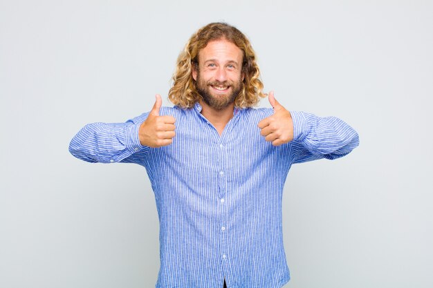 Photo blonde man smiling broadly looking happy, positive, confident and successful, with both thumbs up