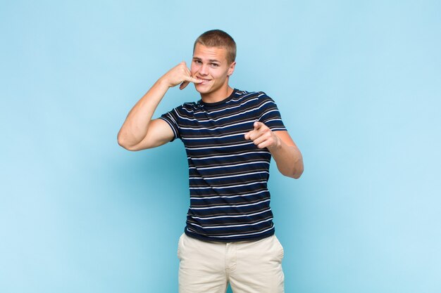 Blonde  man smiling cheerfully and pointing to front while making a call you later gesture, talking on phone