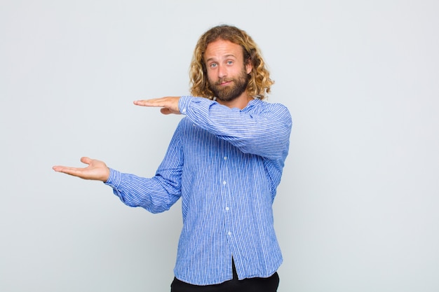 Photo blonde man smiling, feeling happy, positive and satisfied, holding or showing object or concept