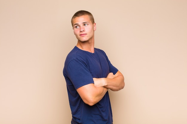 Blonde  man smiling gleefully, feeling happy, satisfied and relaxed, with crossed arms and looking to the side