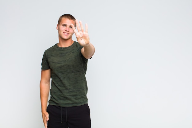 Blonde  man smiling and looking friendly, showing number four or fourth with hand forward, counting down