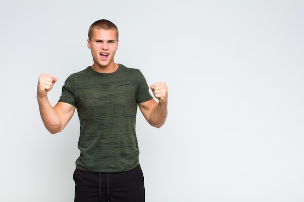 Blonde man voelt zich blij, verrast en trots, schreeuwt en viert succes met een grote glimlach