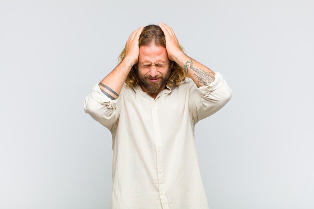 Foto blonde man voelt zich gestrest en angstig, depressief en gefrustreerd door hoofdpijn, beide handen naar het hoofd opgeheven